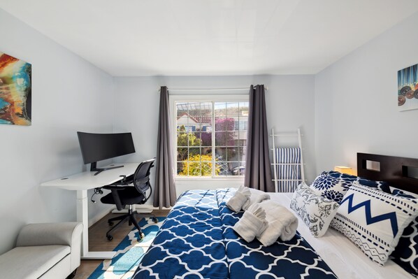 Ein Schlafzimmer mit Bett, Schreibtisch, Stuhl, Fernseher und einem Fenster mit Vorhängen.