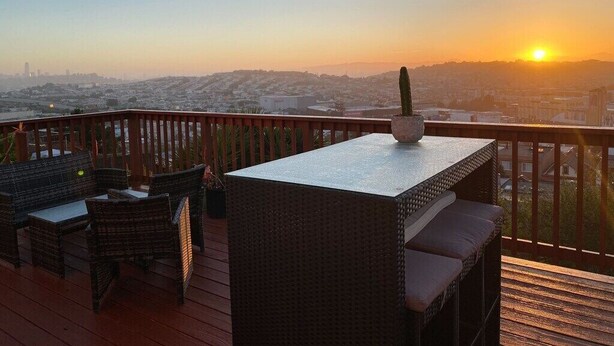 A deck with wicker furniture and a table, overlooking a cityscape during sunset. - SF Home with SPECTACULAR VIEW- Minutes to downtown (San Francisco)