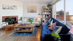 A modern living room with a fireplace, a blue sofa, a coffee table, and a bookshelf. - SF Home with SPECTACULAR VIEW- Minutes to downtown (San Francisco)
