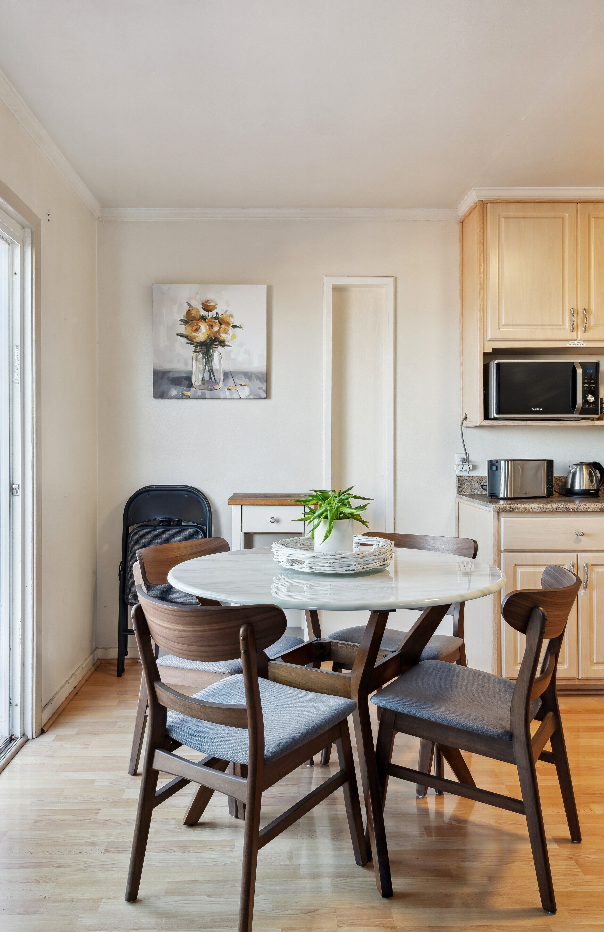 A dining area with a round table, four chairs, a potted plant, and a microwave in the background.