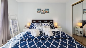A neatly made bed with blue and white patterned bedding, two bedside lamps, a small bedside table with a lamp, and a wall-mounted artwork above the bed. - SF Home with SPECTACULAR VIEW- Minutes to downtown (San Francisco)