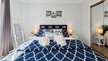 A neatly made bed with blue and white patterned bedding, two bedside lamps, a small bedside table with a lamp, and a wall-mounted artwork above the bed.