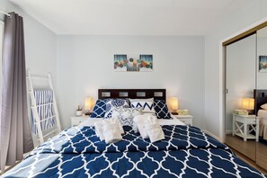 A neatly made bed with blue and white patterned bedding, two bedside lamps, a small bedside table with a lamp, and a wall-mounted artwork above the bed.