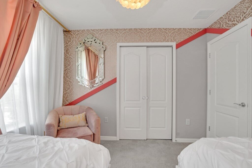 A bedroom with two beds, a large mirror, a wardrobe, and a red accent wall.