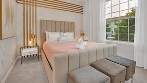 A modern bedroom with a large bed, bedside lamps, a bench, and a view of the outside. - 5 Bedroom  Home 8 Minutes To Disney and Parks (Kissimmee)