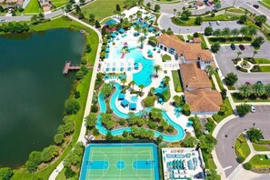 Luchtbeeld van een resort met een groot zwembad, een tennisbaan en een steiger aan een meer.