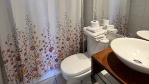 Ein Badezimmer mit Toilette, Waschbecken, einer Duschkabine mit Blumenmuster und einem Spiegel.
