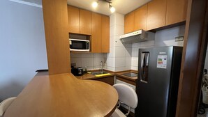 Eine kleine Küche mit Holzschränken, einem Edelstahlkühlschrank, einer Mikrowelle, einem Spülbecken und einem kleinen Esstisch mit zwei Stühlen.