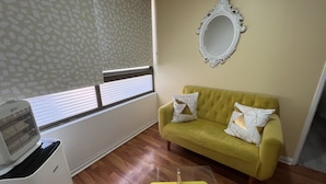 Ein Zimmer mit einem gelben Sofa, einem weißen Zier-Spiegel, einer durchsichtigen Kunststoff-Aufbewahrungsbox und einem weißen Heizgerät.