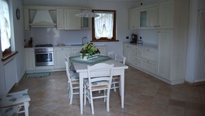 Een keuken met witte kasten, een eettafel met stoelen, een fornuis en een raam met gordijnen.