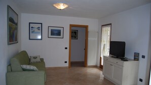 Een woonkamer met een groene bank, een televisie op een kast, en ingelijste foto’s aan de muur.