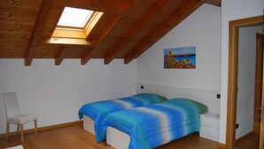 Een slaapkamer met dakraam, een bed met blauw beddengoed, een stoel en een schilderij aan de muur.