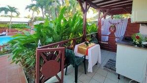 Un espace extérieur abrité comprenant une piscine, des chaises vertes, une table recouverte d’une nappe blanche et un barbecue.