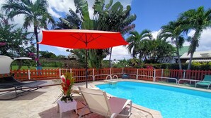 Un espace piscine agrémenté d’un parasol rouge, de chaises longues et d’une terrasse carrelée.