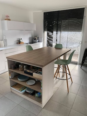 Una cocina moderna con una isla de madera, sillas verdes y un ventanal corredero al exterior.