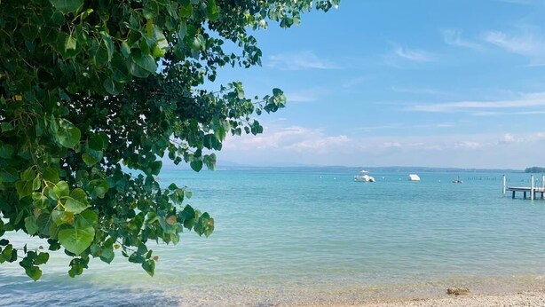Ein freier Blick auf einen Strand mit ruhigem Wasser, einem Kiesstrand und einem in der Ferne liegenden Steg.