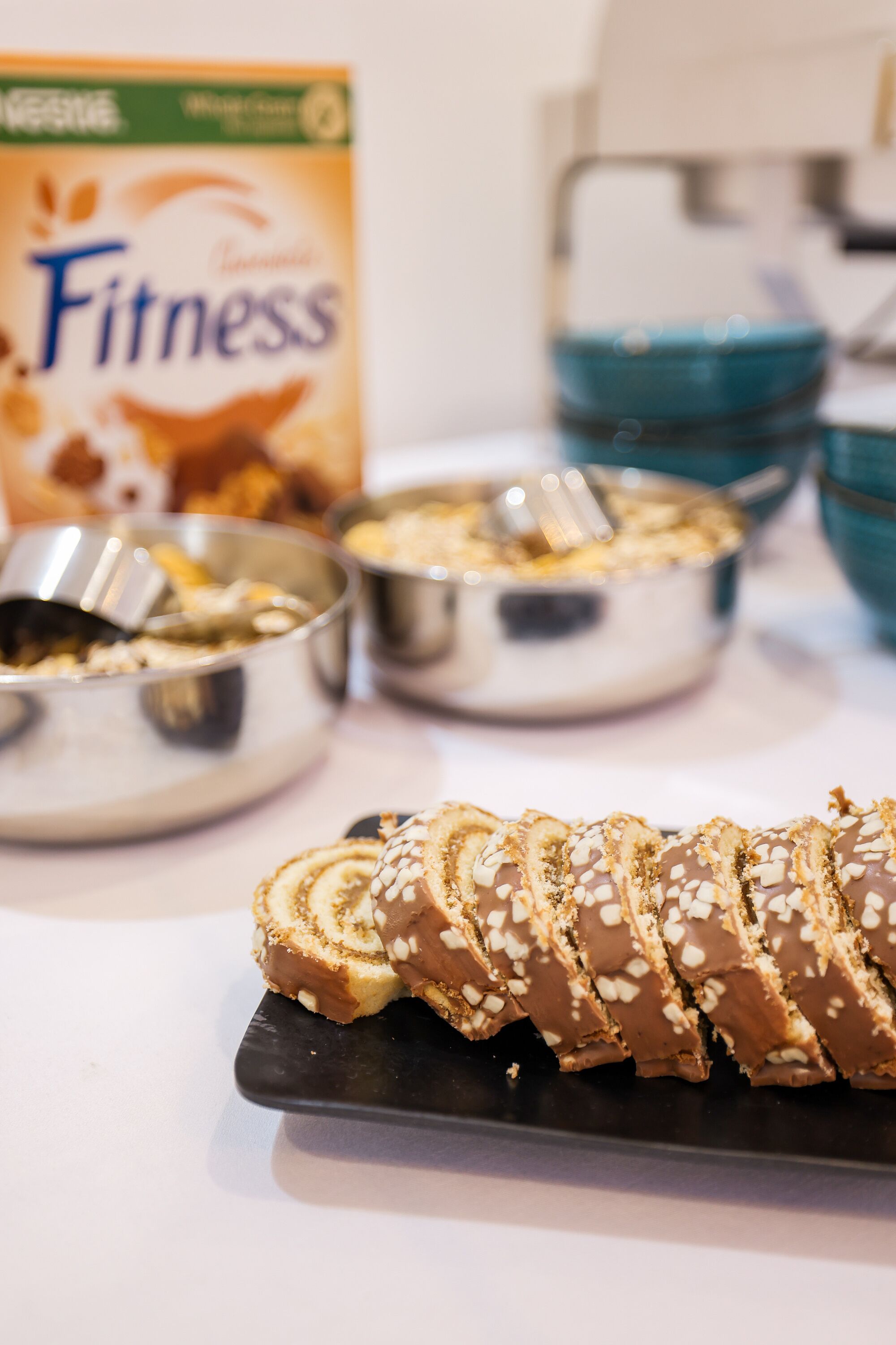 Een schaal met plakjes gebak, bestrooid met sesamzaad, en een doosje met de tekst 'Fitness' op de achtergrond.