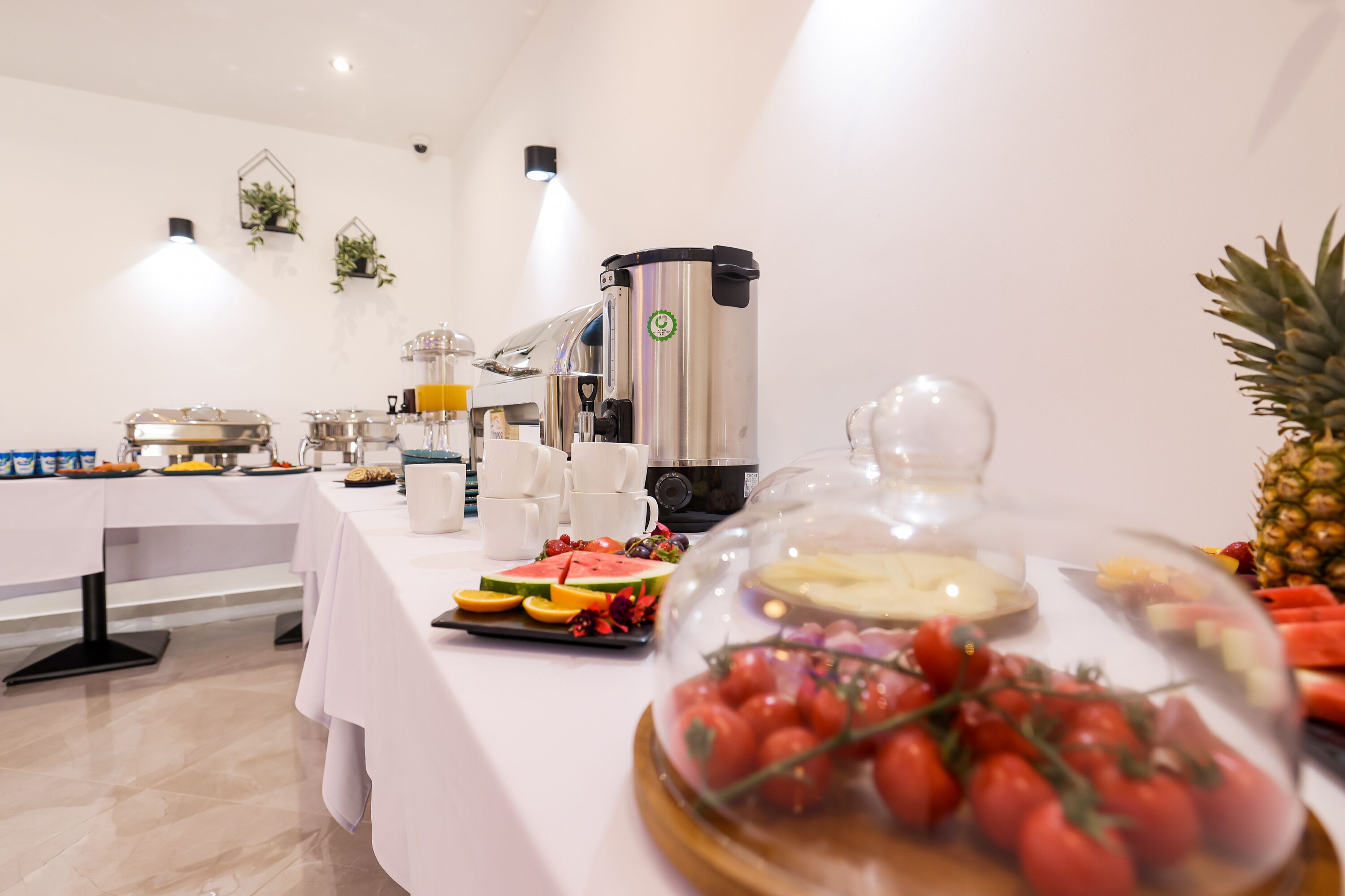 Disposição de buffet com diversos alimentos, uma máquina de café e uma abacaxi decorativa.