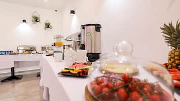 Disposição de buffet com diversos alimentos, uma máquina de café e uma abacaxi decorativa.