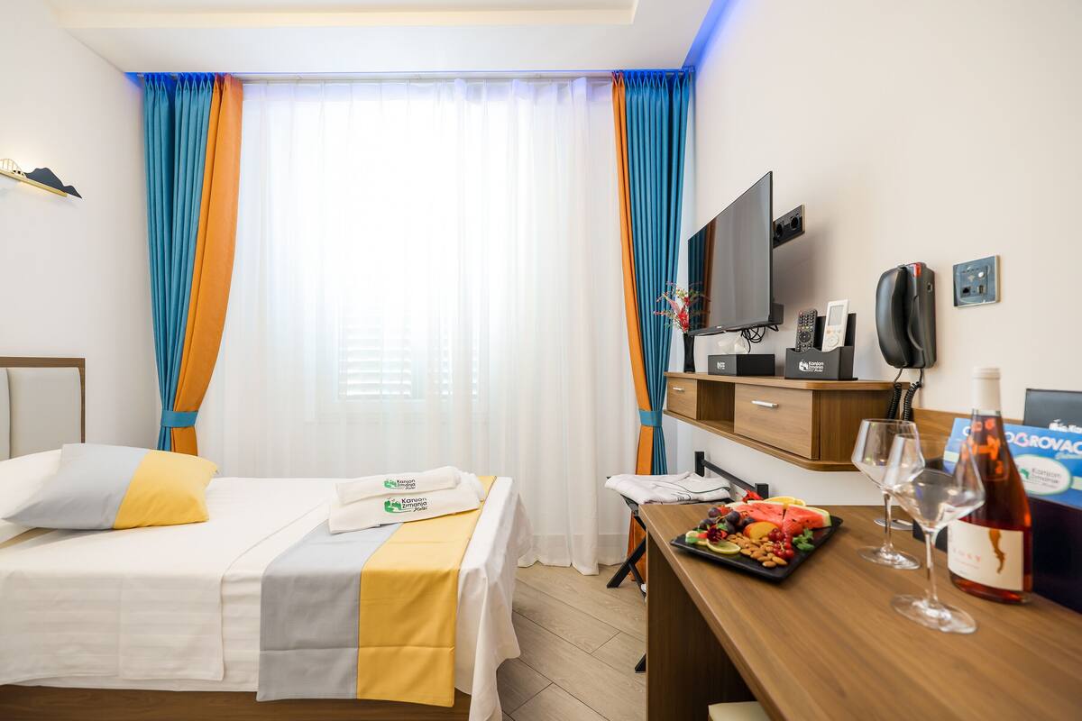 Une chambre d’hôtel comprenant un lit, un bureau avec un plateau de fruits et des verres à vin, une télévision et un mini-bar.