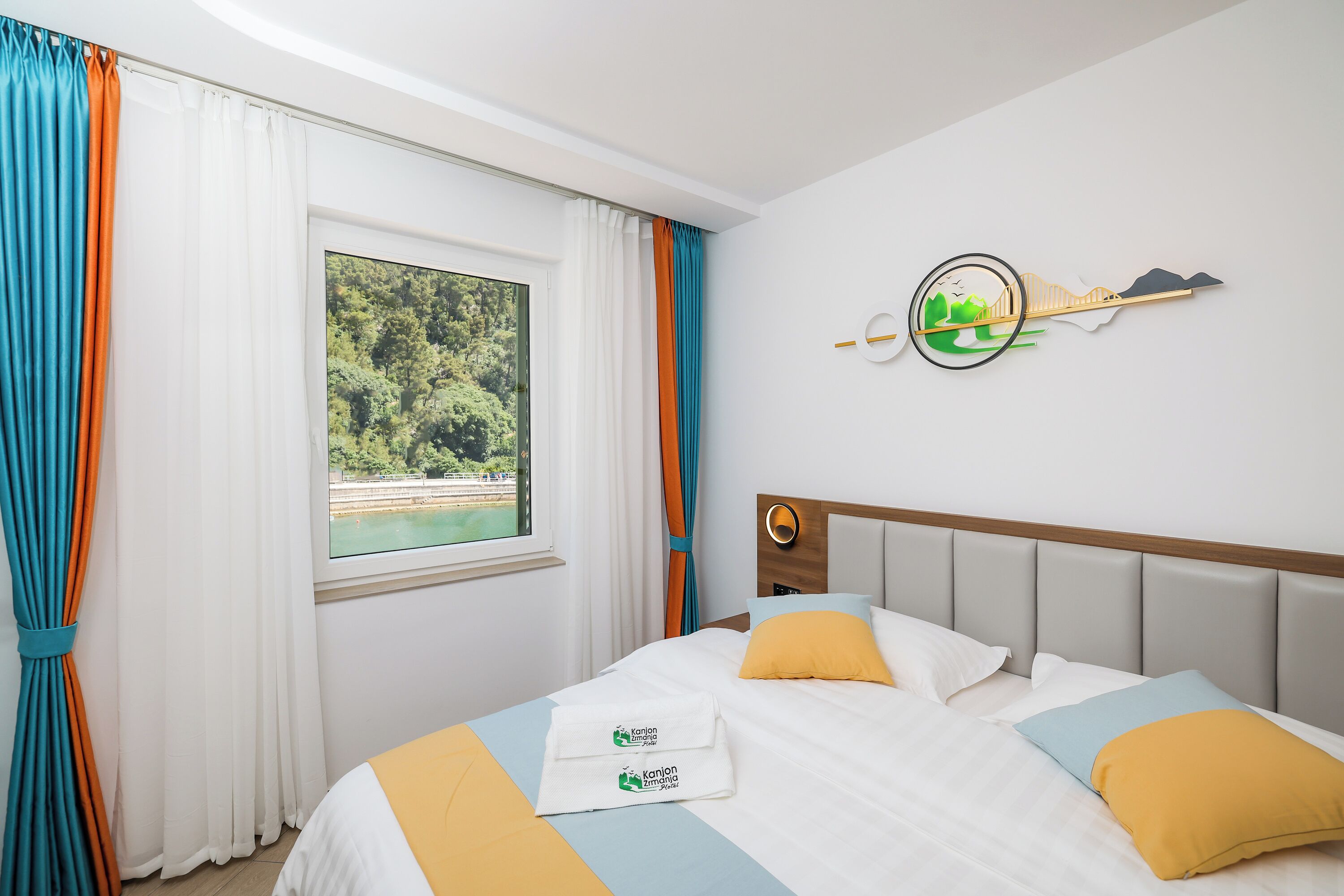 Een hotelkamer met een bed, een raam met gordijnen, een wanddecoratie en een bedspreide met handdoeken.