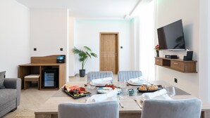 A modern hotel room with a dining area, a TV mounted on the wall, a small refrigerator, and a potted plant. - Hotel Kanjon Zrmanje (Obrovac)