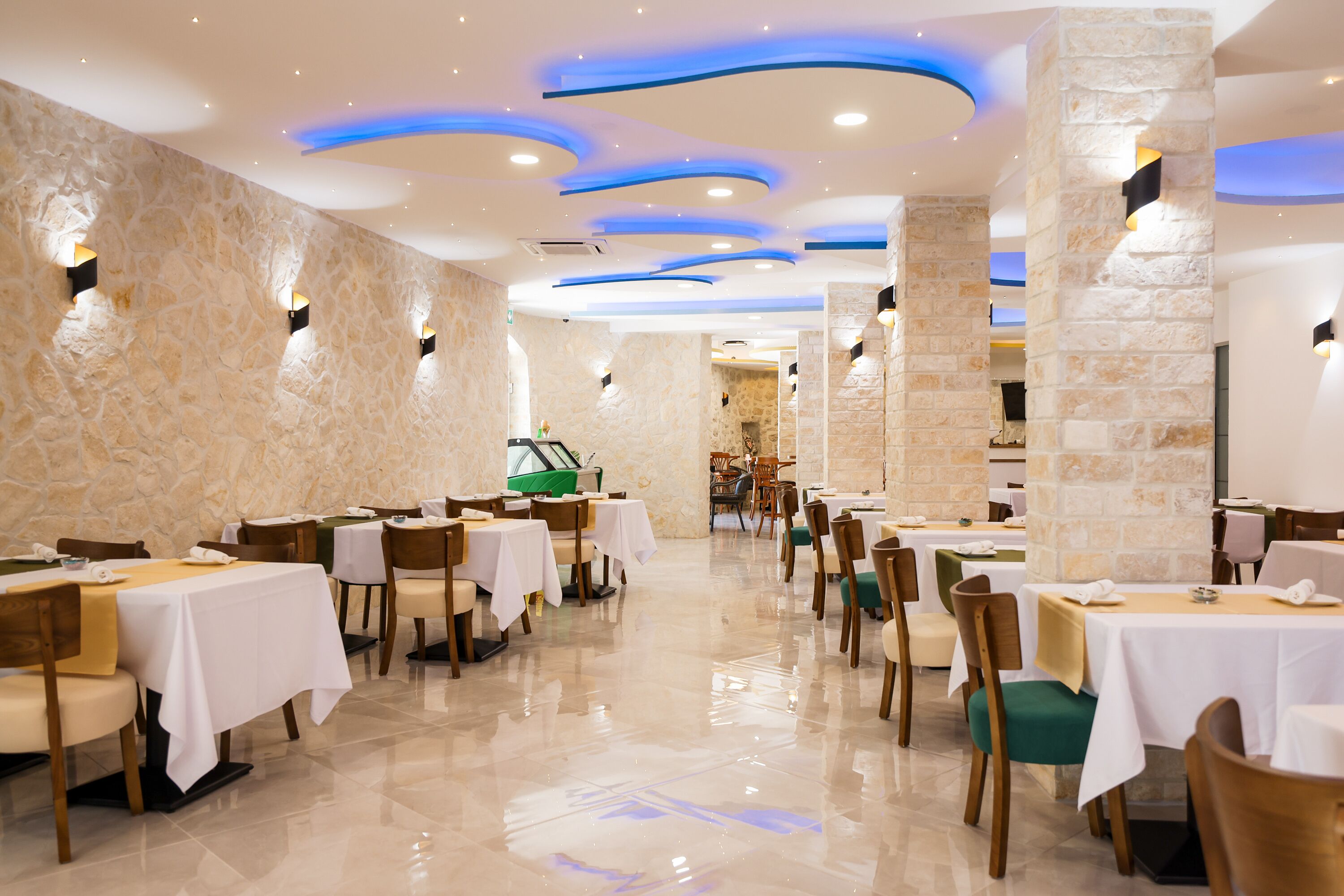 A restaurant with multiple tables and chairs, stone walls, and modern lighting fixtures.