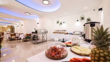Un espace de restauration moderne dans un hôtel, avec des tables recouvertes de nappes blanches, un coin café et un buffet proposant une variété de plats.