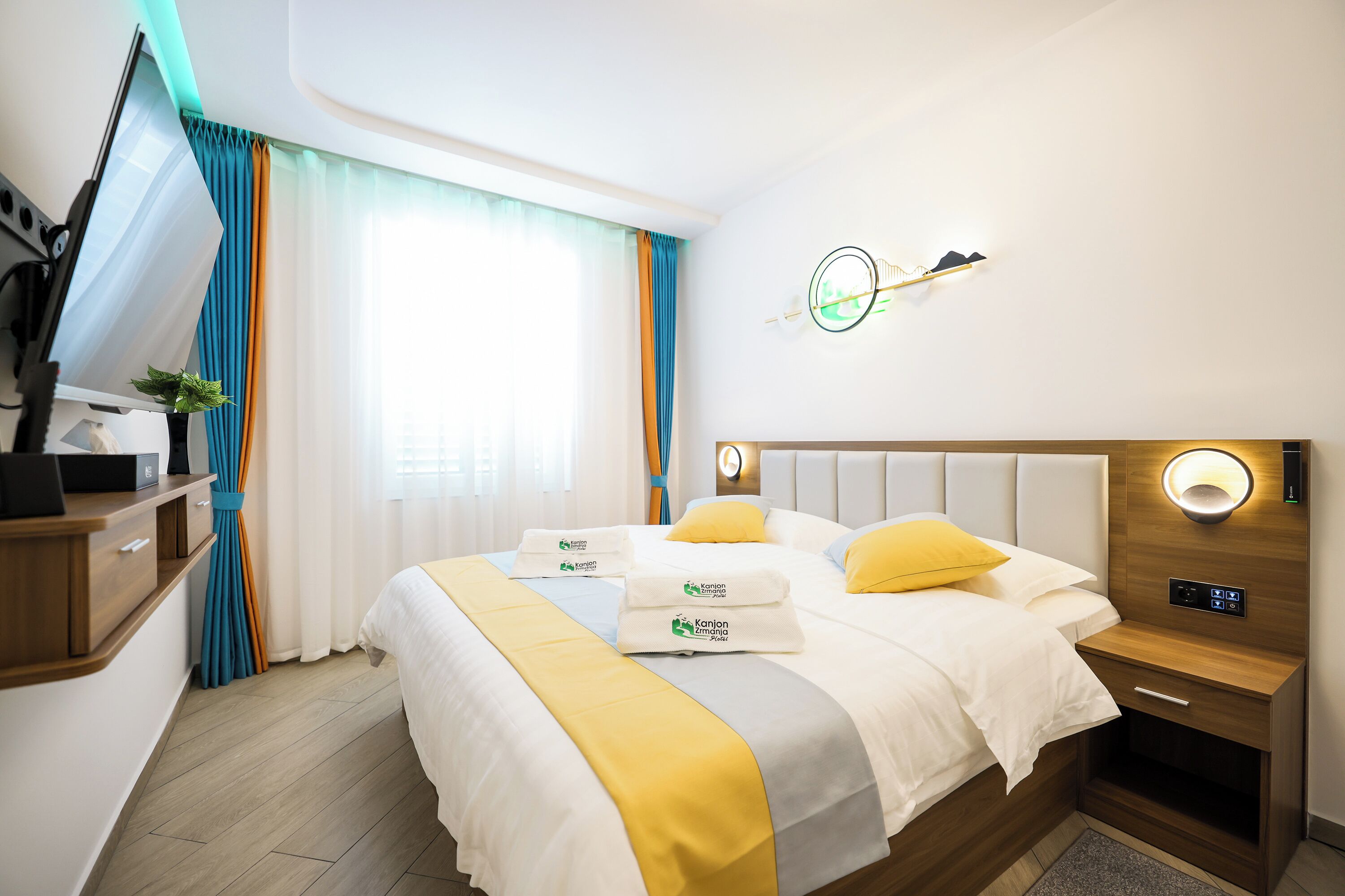 A hotel room with a bed, bedside tables, a desk, and a window with curtains.