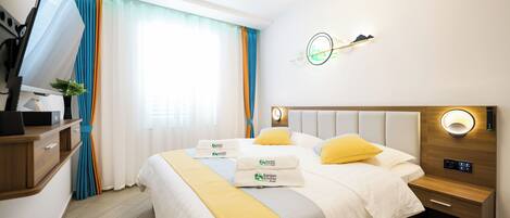 A hotel room with a bed, bedside tables, a desk, and a window with curtains.