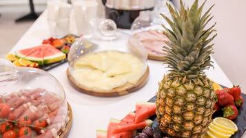 Une table de buffet proposant divers aliments, notamment un ananas, une pastèque, des raisins et du fromage.