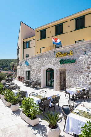 An outdoor cafe area with tables and chairs, a stone wall, and a flag. - Hotel Kanjon Zrmanje (Obrovac)