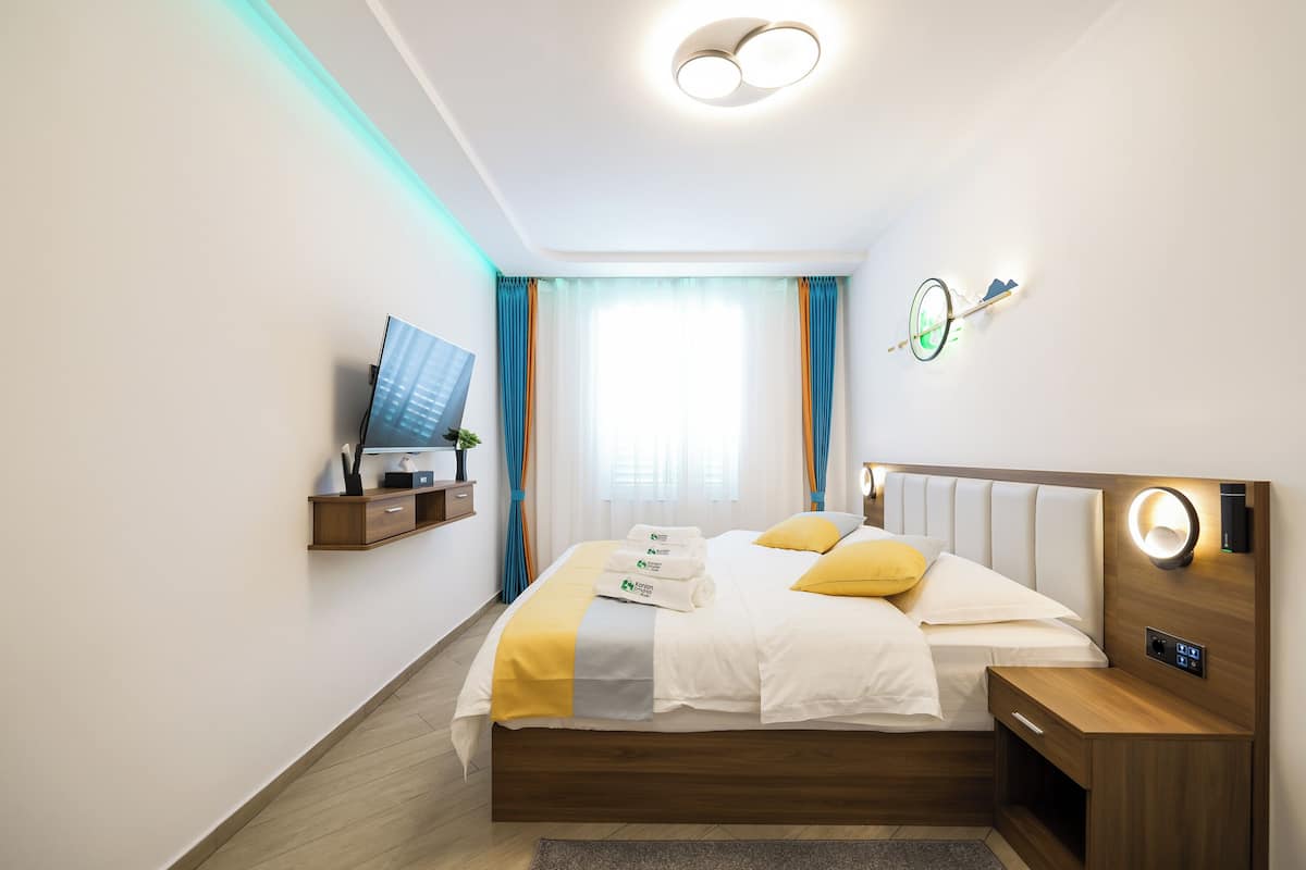 Une chambre d’hôtel moderne équipée d’un lit, d’une table de chevet, d’un téléviseur fixé au mur et d’un luminaire au plafond.