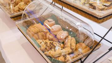 Un bufé con diversas opciones de panadería bajo campanas de vidrio, incluyendo pasteles y pan.