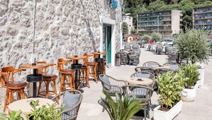 An outdoor café with wicker furniture and potted plants, a stone wall, and a clear blue sky. - Hotel Kanjon Zrmanje (Obrovac)