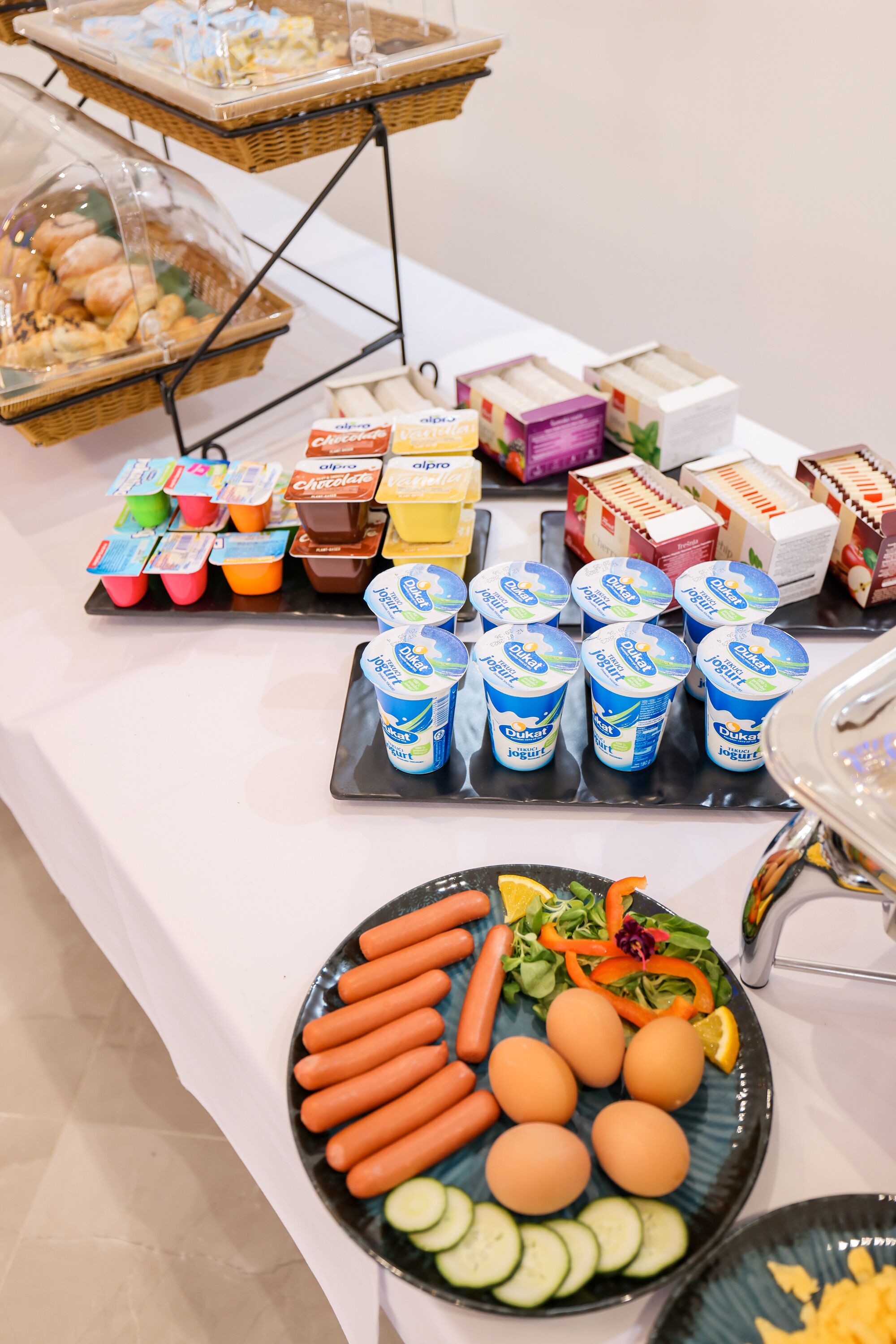 A buffet table with various food items including yogurt cups, pastries, and a plate with eggs, carrots, and vegetables.