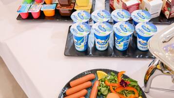 A buffet table with various food items including yogurt cups, pastries, and a plate with eggs, carrots, and vegetables.