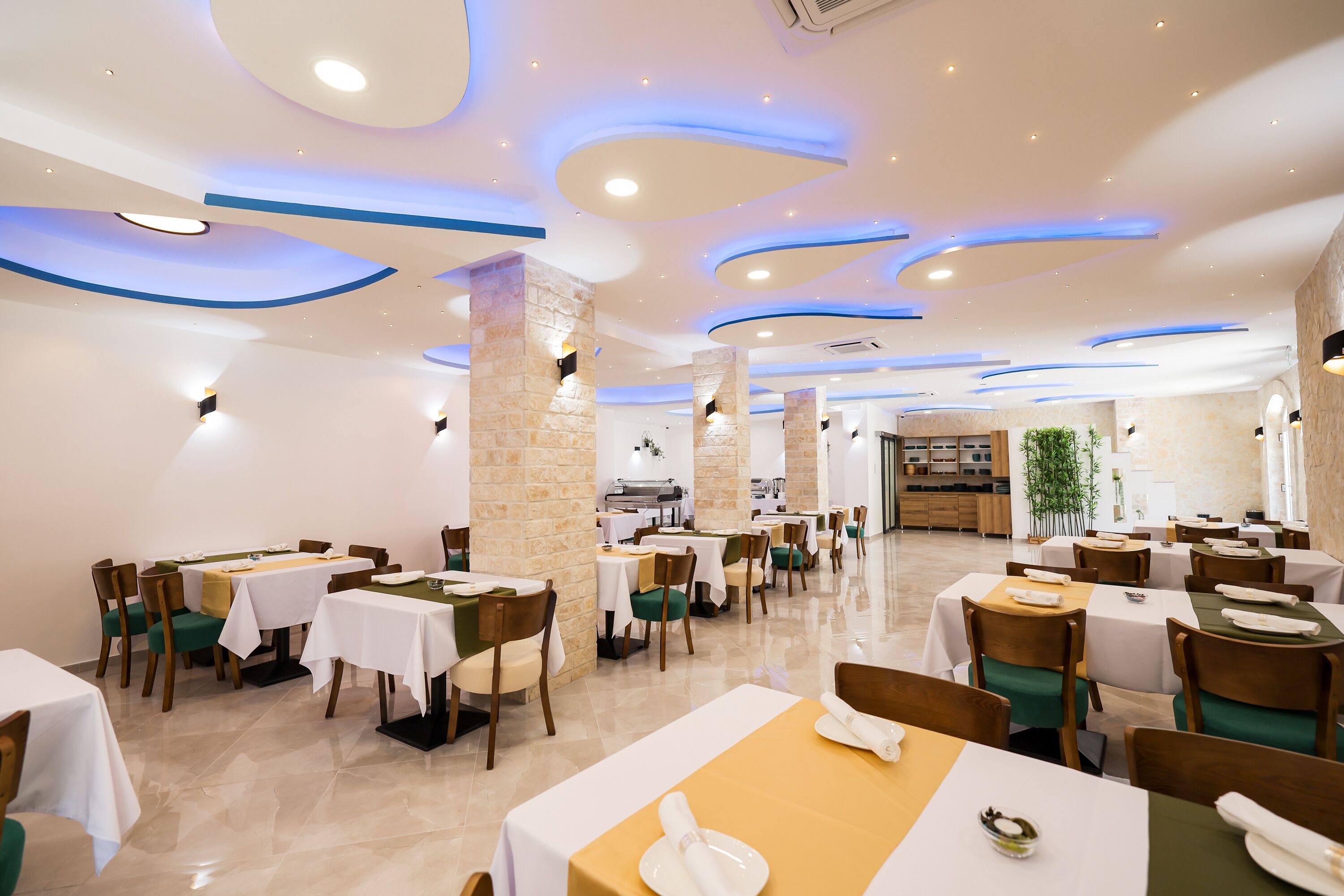 A restaurant with multiple tables and chairs, a stone pillar, and a kitchen area in the background.