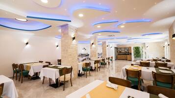 A restaurant with multiple tables and chairs, a stone pillar, and a kitchen area in the background.