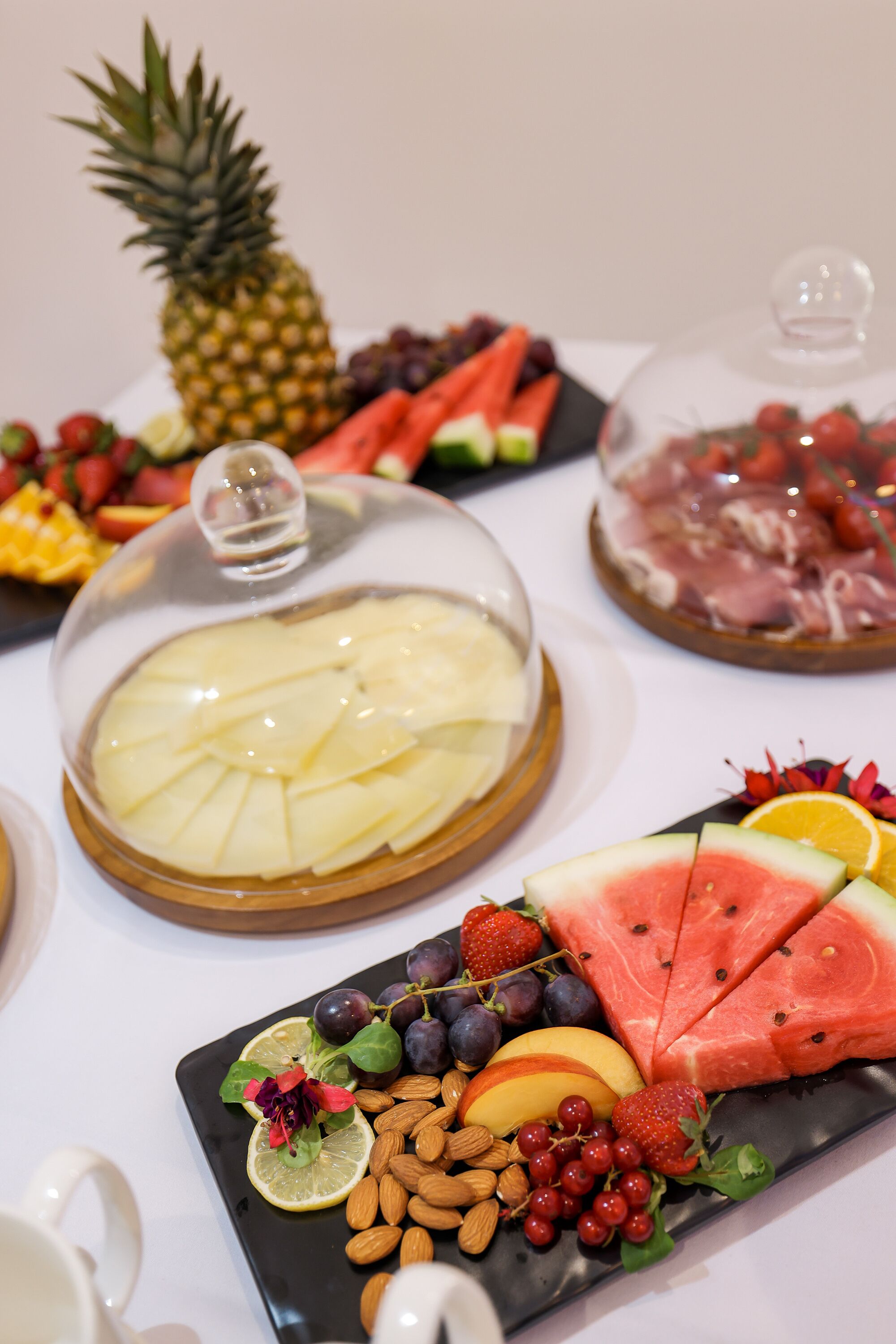 Una mesa con frutas y quesos variados, incluyendo piña, sandía y almendras.