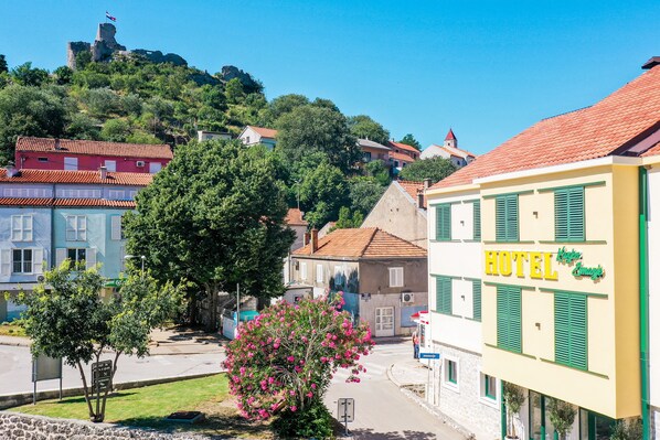 A hotel with a sign reading "HOTEL" in yellow letters, surrounded by buildings with red-tiled roofs and green shutters. - Hotel Kanjon Zrmanje (Obrovac)