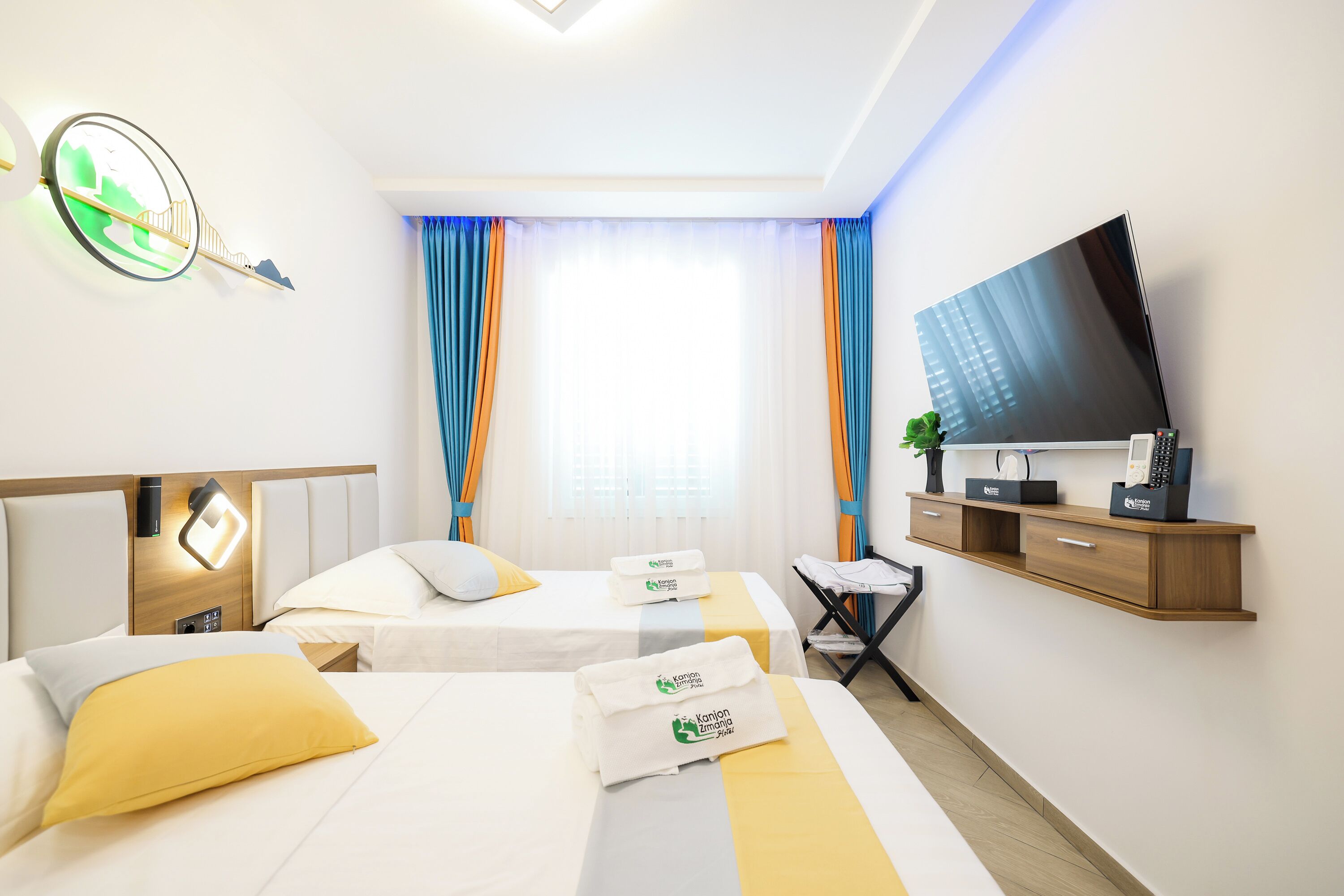 A hotel room with two beds, a flat-screen TV, a desk with a chair, and a window with curtains.