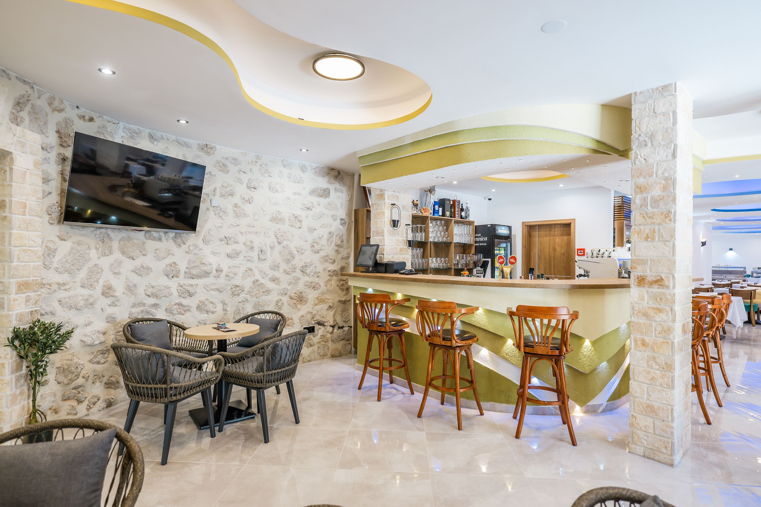 A modern bar area with stone walls, a flat-screen TV, wicker chairs, and a counter with bar stools.