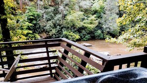 A hot tub on a wooden deck with a river and forest in the background. - A River Retreat is an Authentic A-Frame with 200' frontage on the Toccoa River (Blue Ridge)