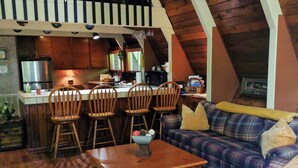 A cozy loft-style living space with a kitchen, wooden floors, and a high ceiling. - A River Retreat is an Authentic A-Frame with 200' frontage on the Toccoa River (Blue Ridge)