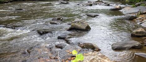 Un río con rocas y una estructura de madera al fondo.