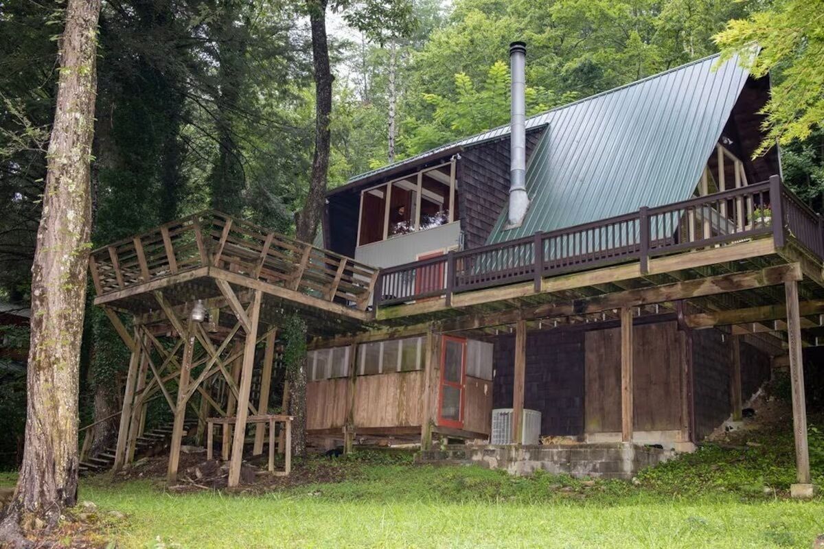 Une cabane dotée d’une terrasse en bois, d’un toit en métal et d’une cheminée.