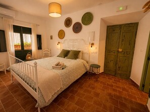Un dormitorio con cama, mesita de noche, lámpara, un reloj de pared y una puerta verde.