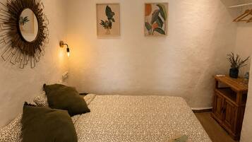 Una camera da letto con un letto, cuscini, uno specchio fissato al muro e due opere d'arte incorniciate.