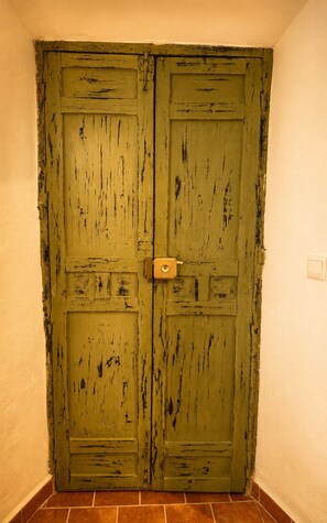 Une porte à deux battants en bois, dotée d’une poignée en laiton, est encastrée dans un coin et surplombe un sol carrelé.
